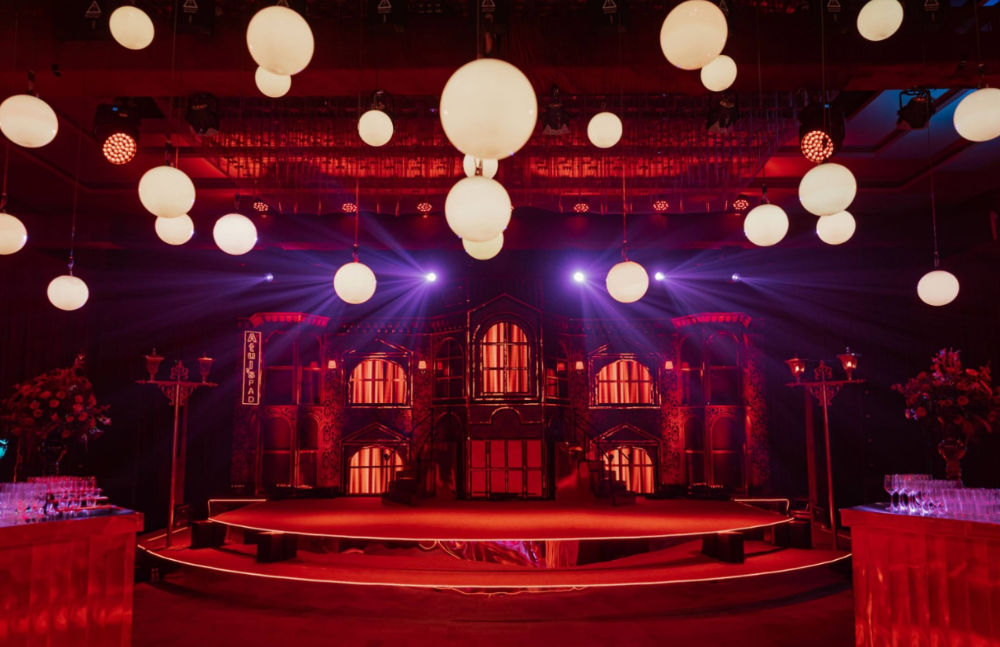 Elegant event venue with red lighting, glowing ceiling orbs, and an ornate stage, creating a sophisticated atmosphere.