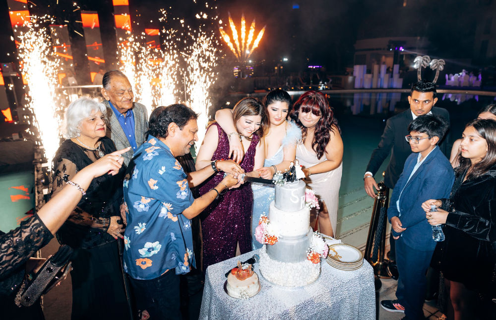 People celebrate with a cake and fireworks at a nighttime party by the pool.