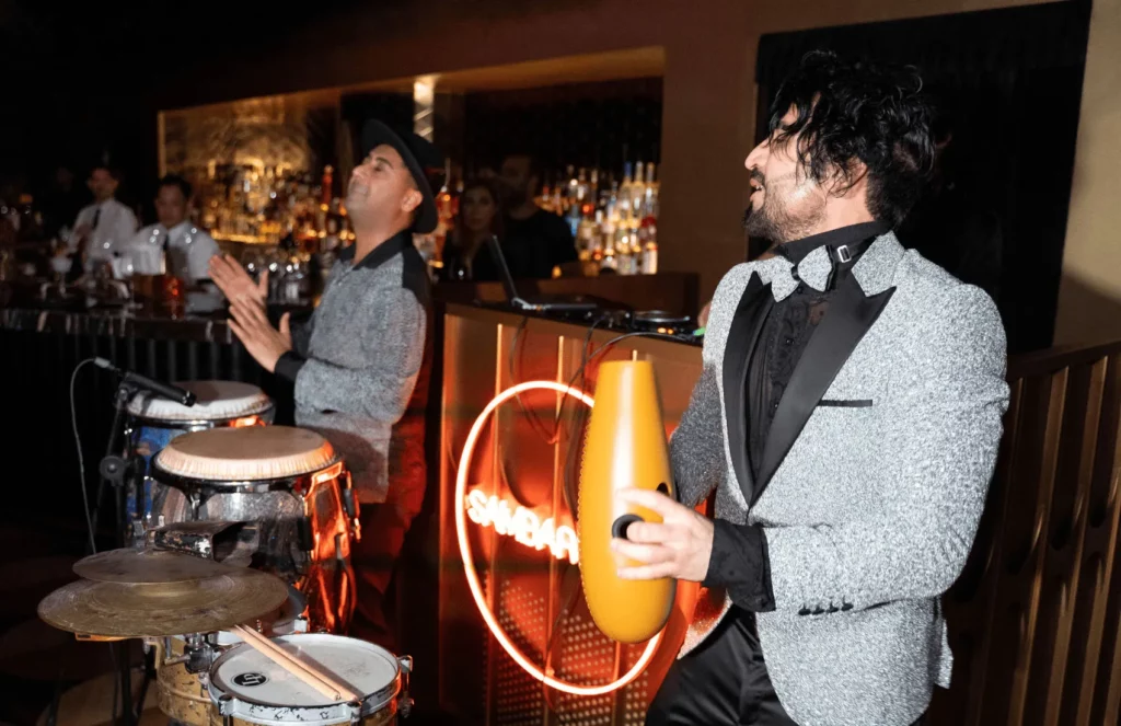Live band performing in a dimly lit bar, musicians playing percussion instruments energetically.