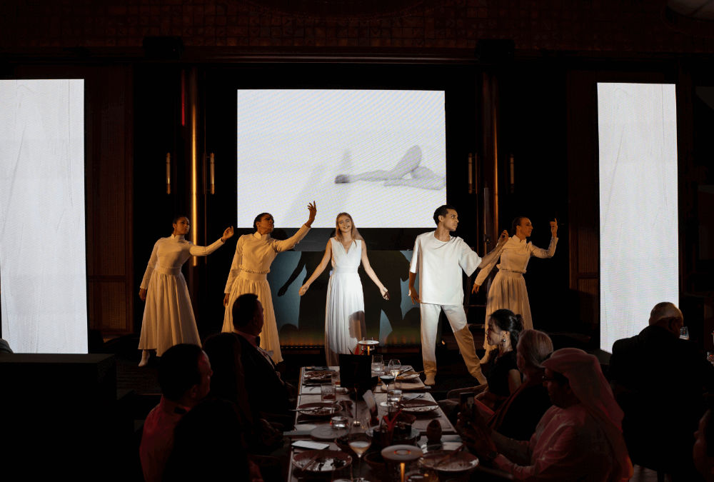 Performance on stage with dancers in white costumes, set against a dramatic backdrop at an indoor event.