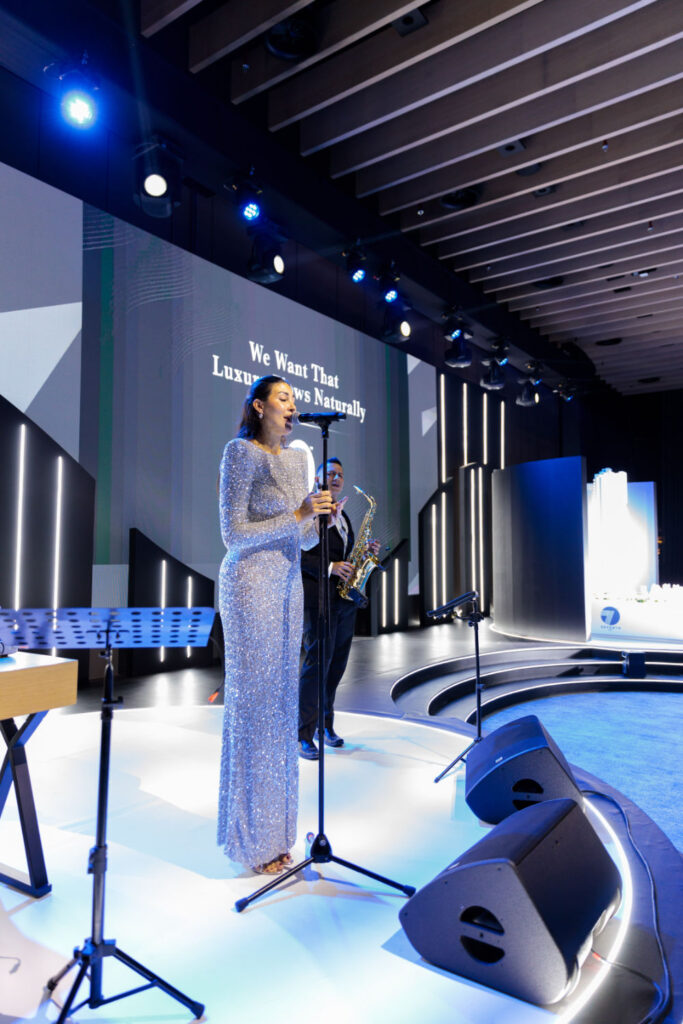 Singer in glittering dress performs with saxophonist on stage under blue lights.