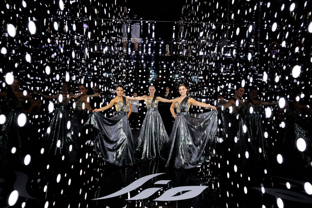 Dancers in silver gowns pose in a reflective, light-filled display, creating mesmerizing visual effects.