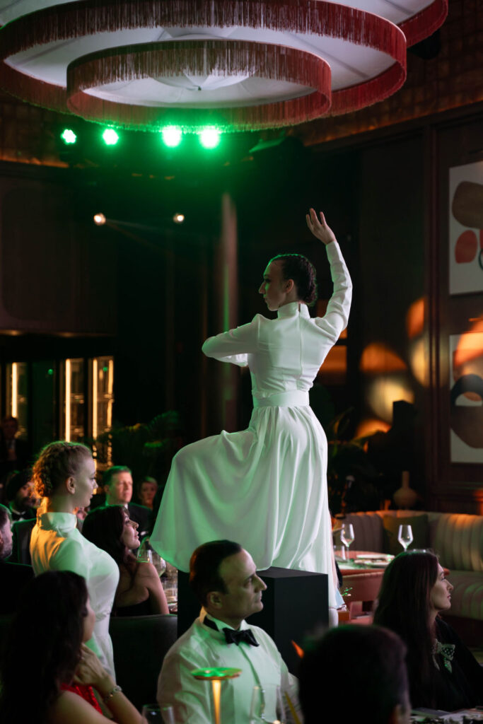 Elegant dancer performs in white dress at a sophisticated dinner event under green lights.