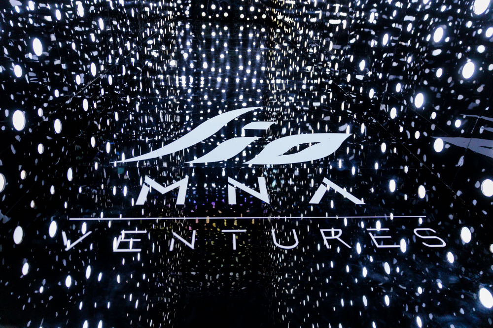 Futuristic illuminated space with MNA Ventures logo on floor, surrounded by glowing dots creating a galaxy effect.