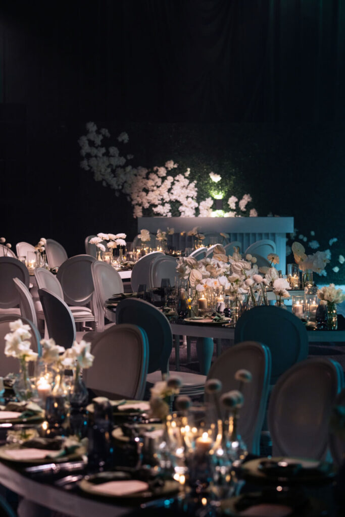 Elegant event dining setup with candlelit tables, white floral decor, and soft lighting ambiance.