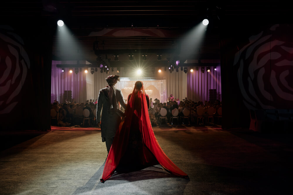 Bride and groom walking into a dimly lit venue, spotlight illuminating them from behind.