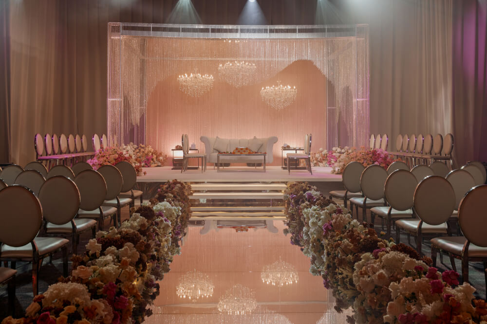 Elegant wedding venue with floral aisle, chandelier, and chic seating arrangement. Luxurious decor and ambiance.