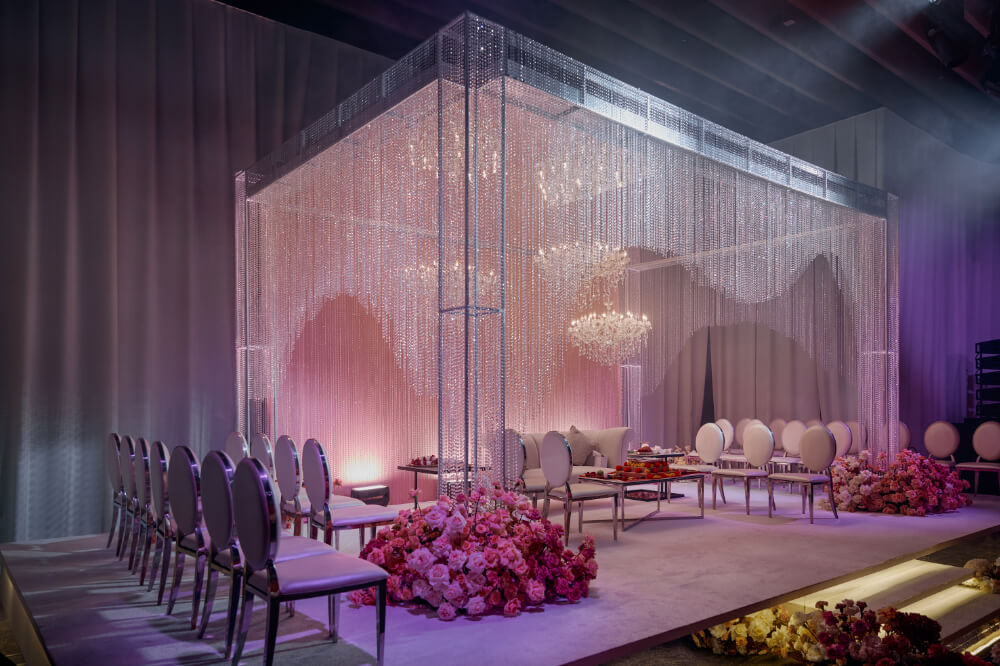Elegant wedding venue with crystal chandeliers, floral arrangements, and modern seating under soft ambient lighting.