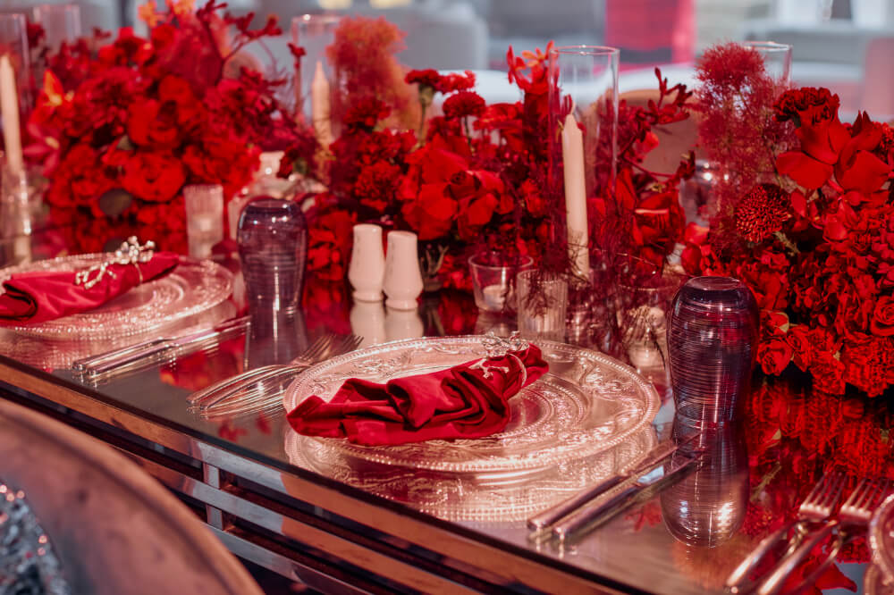 Elegant table with red floral decor, silver plates, burgundy napkins, and glassware, perfect for a romantic dinner.