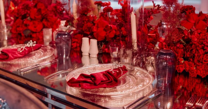 Elegant red-themed dining table with floral centerpiece, ornate plates, and folded napkins for a festive celebration.