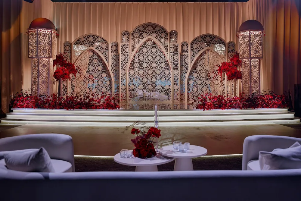Elegant wedding stage with floral décor, intricate backdrop, and cozy seating arrangement in warm lighting.