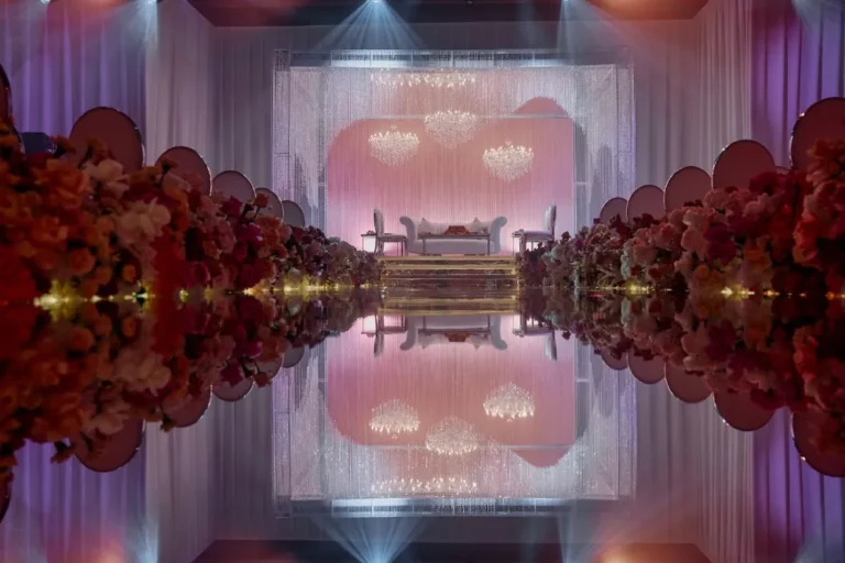 Luxurious wedding stage with chandeliers and floral decorations reflecting on glossy floor.