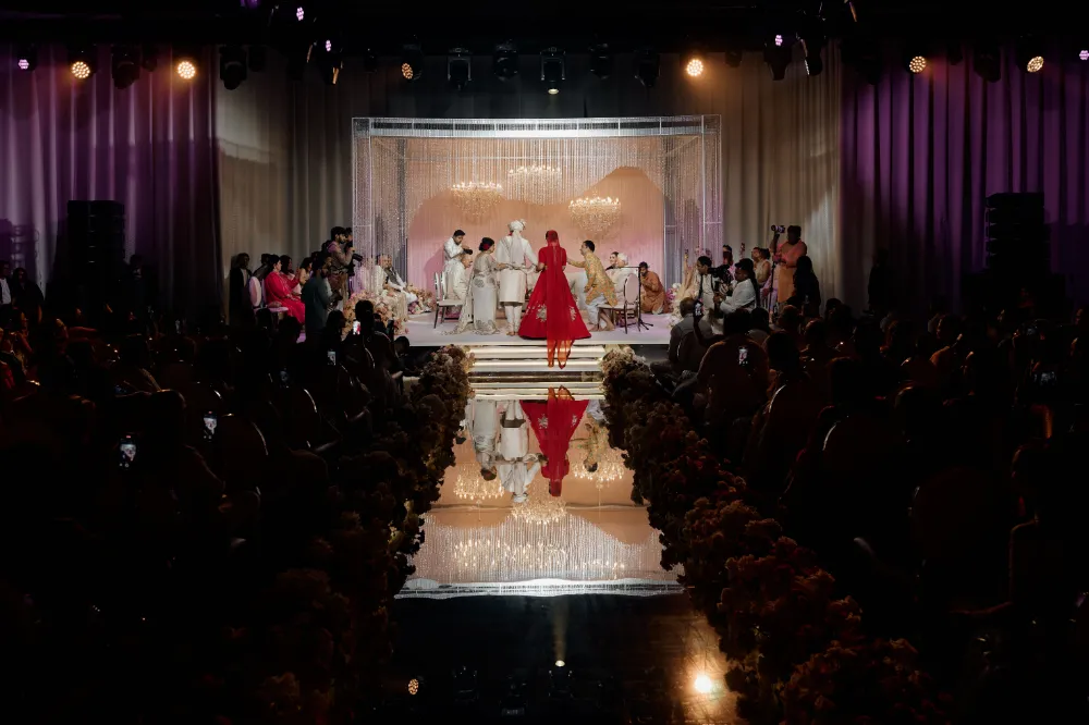 Elegant wedding ceremony with guests in a dimly lit venue, featuring a person in a red dress walking towards the stage.