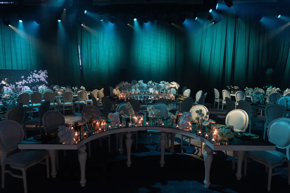 Elegant event hall with dim lighting, decorated tables, and white chairs set for an evening banquet or celebration.