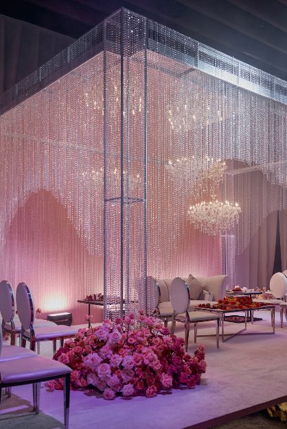 Elegant wedding setup with pink floral arrangements, crystal chandeliers, and ambient lighting under a shimmering canopy.