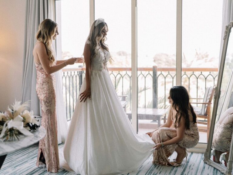 Bride in elegant gown receiving help from bridesmaids in stylish dresses before the ceremony.