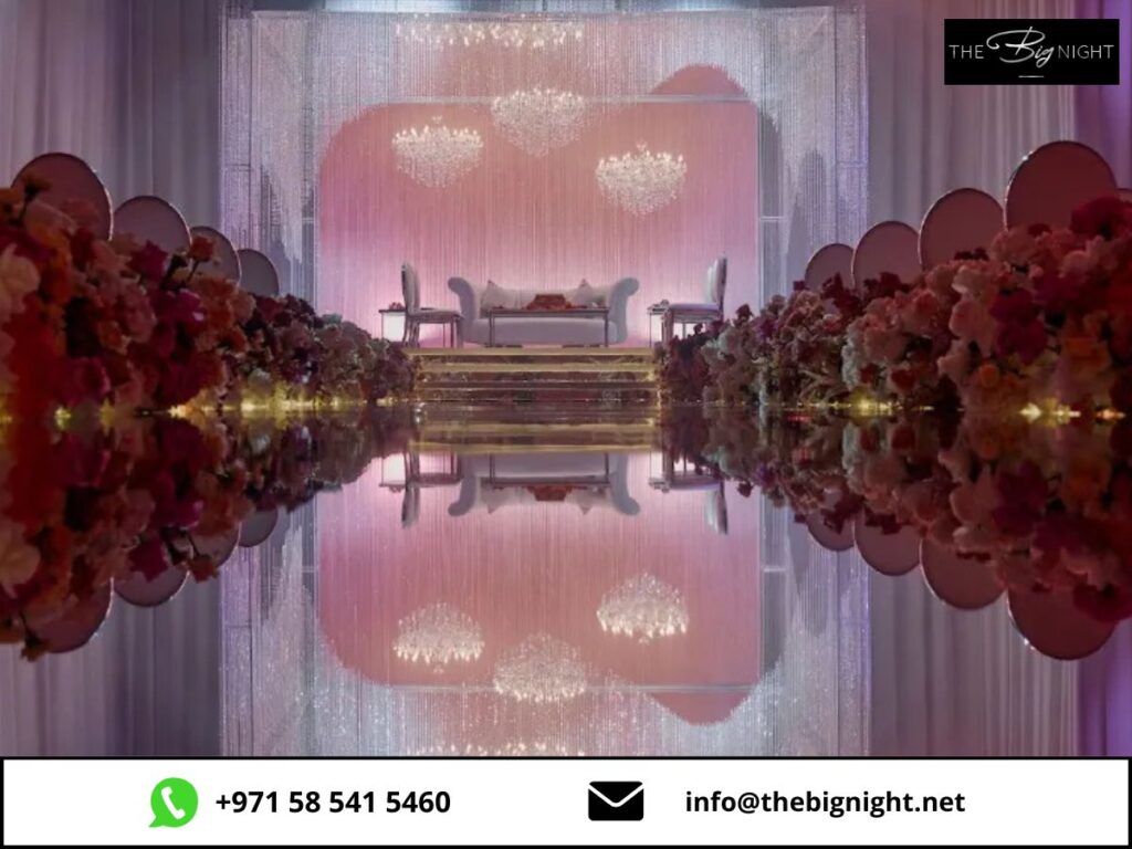 Elegant wedding stage with floral arrangements and chandeliers, featuring stylish seating and soft pink lighting.