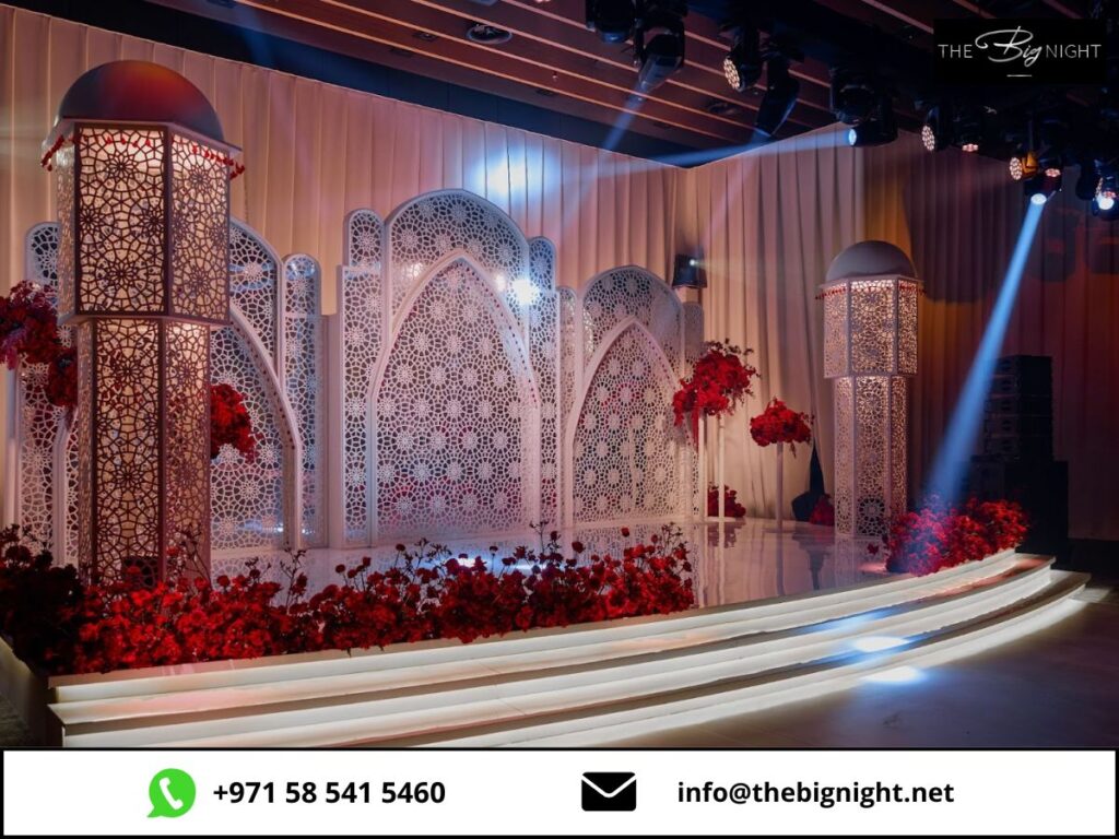 Elegant wedding stage decor with white lattice panels, red flowers, and ambient lighting. Contact: +971 58 541 5460.