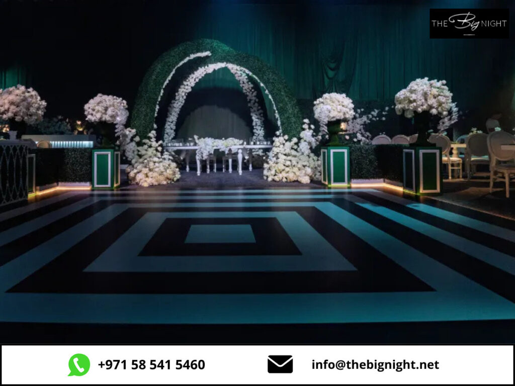 Elegant event setup with floral arch and modern decor, black and white striped floor, contact info at bottom.