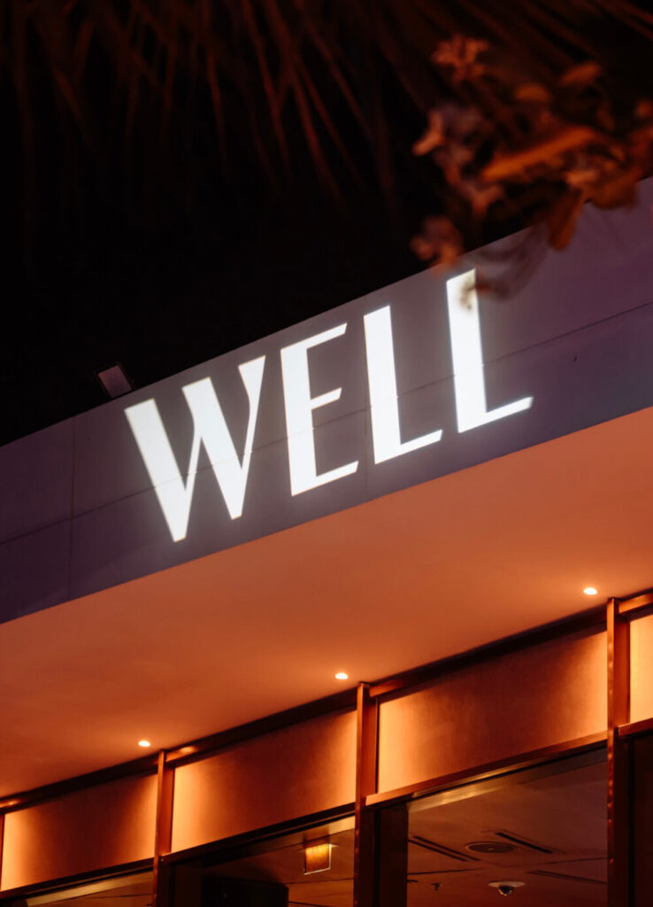 Illuminated 'WELL' sign on a modern building at night with warm lighting