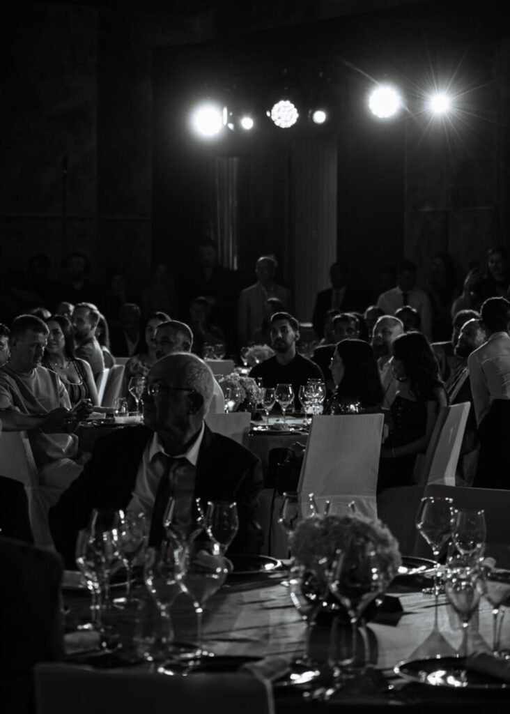 Formal dinner event with people seated at tables under bright stage lights.