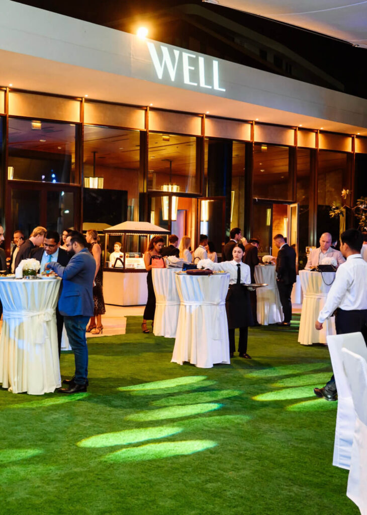 Outdoor evening party at a well-lit venue with standing tables and guests mingling.