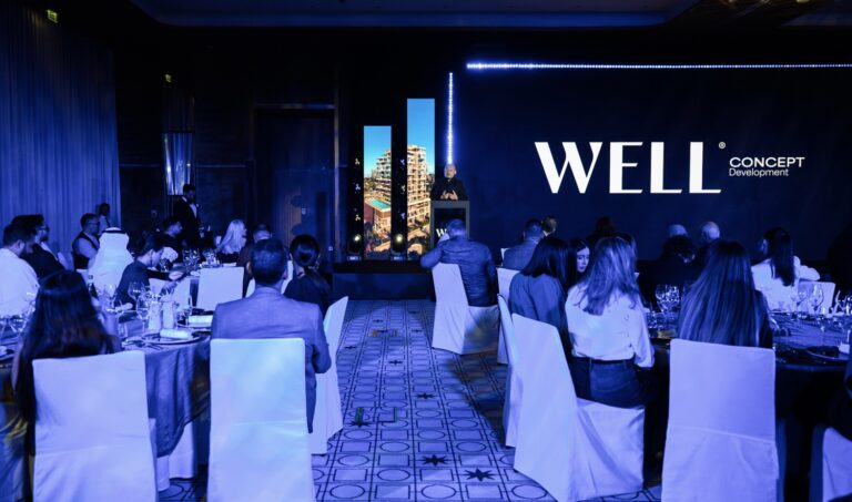 Audience at corporate event with a speaker presenting WELL Concept Development on a large screen.