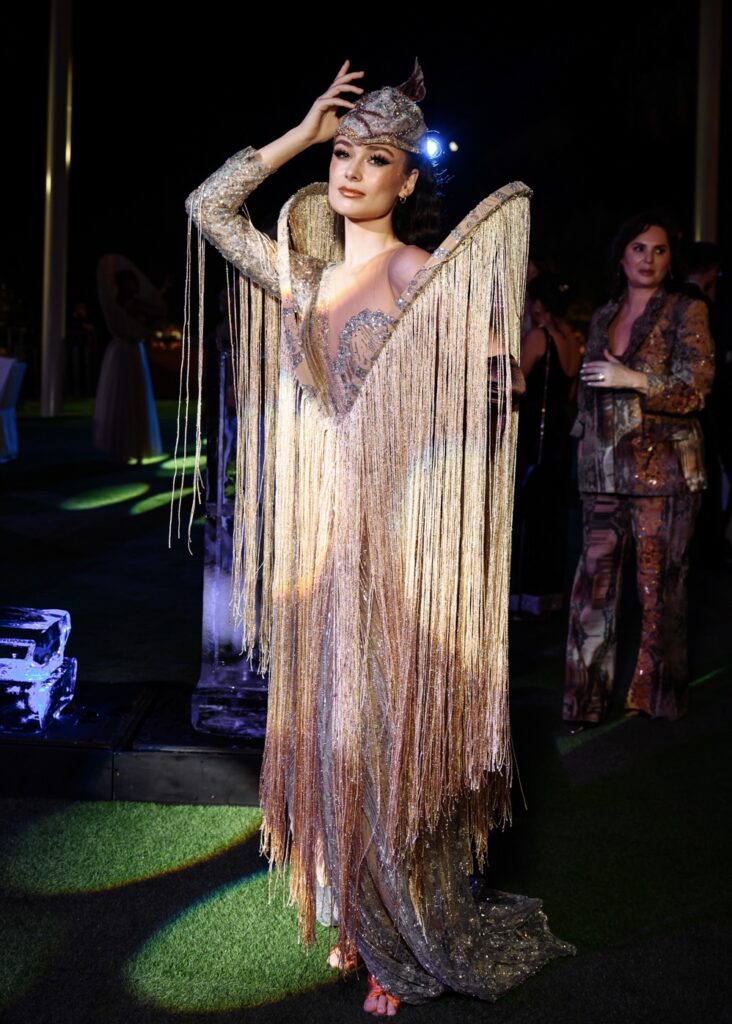 Elegant woman in shimmering fringe dress and ornate headpiece at a glam nighttime event.