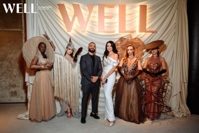 Group at WELL event in elegant fashion, posing in front of draped backdrop with the word WELL illuminated above.