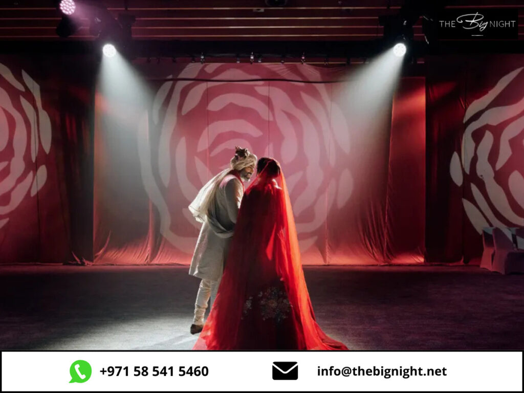 Bride and groom embracing at a beautifully lit wedding stage with rose patterns. Contact The Big Night for inquiries.