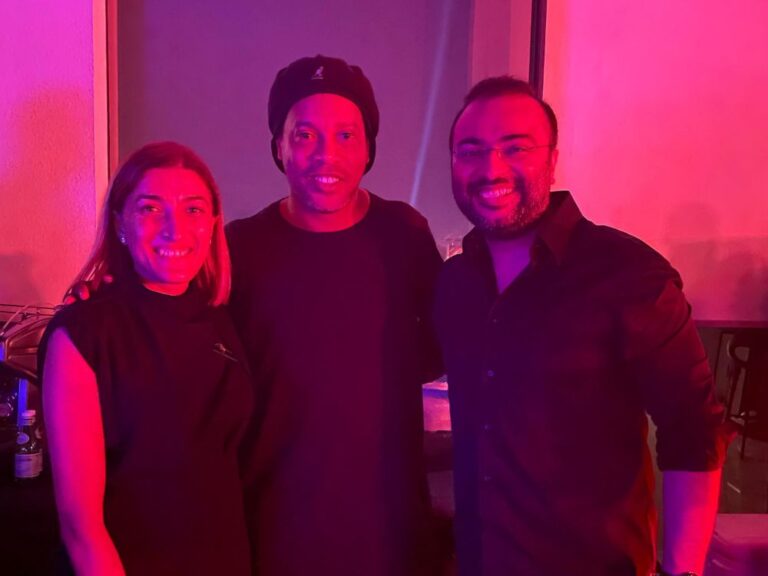 Three people smiling in a dimly lit room with red lighting, dressed in dark clothing.