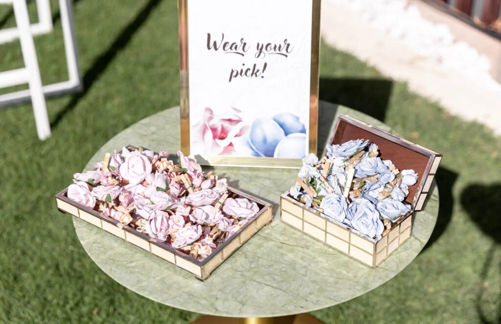 Floral accessories on table with Wear your pick sign at outdoor event. Pink and blue flower options in boxes.
