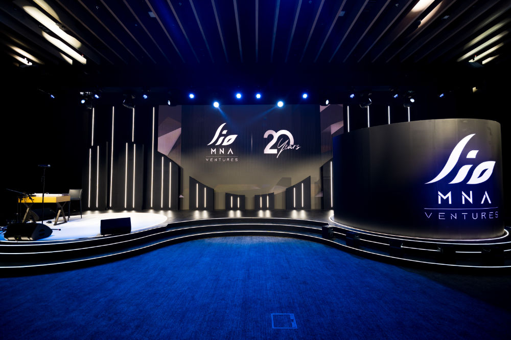 Modern event stage setup with Jio MNA Ventures 20 Years logo, blue lighting, and elegant design elements.