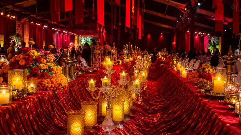 Luxurious banquet hall decorated with red drapes, candles, and floral arrangements for an elegant evening event.